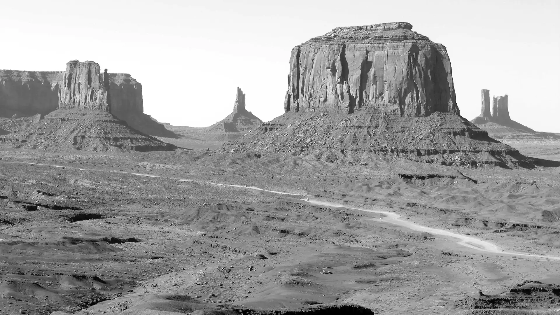 Buttes et pinacles de grès de Monument Valley en noir et blanc, au-dessus de la piste qui traverse la vallée