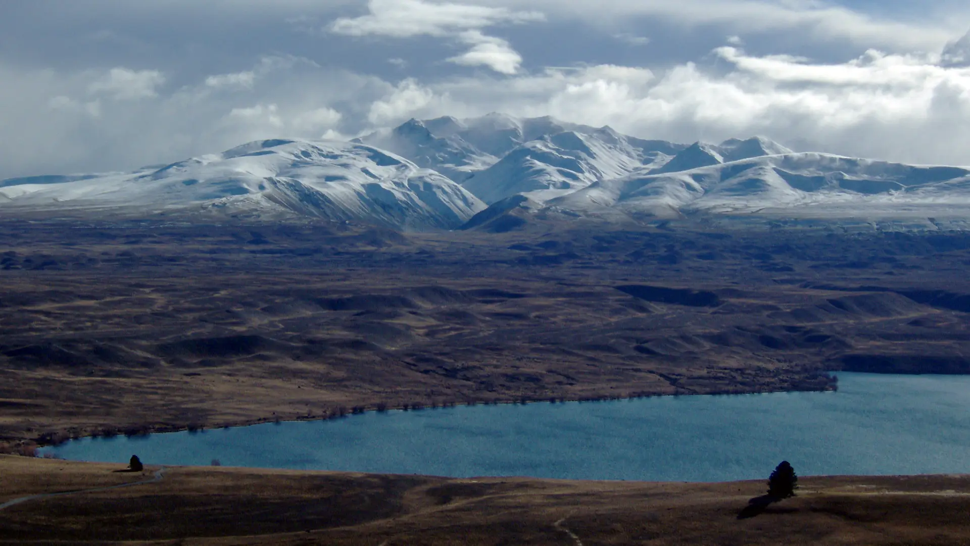 Plaine brune et lac Alexandrina aux eaux bleues au pied des Alpes du Sud enneigées, vus du mont John en Nouvelle-Zélande