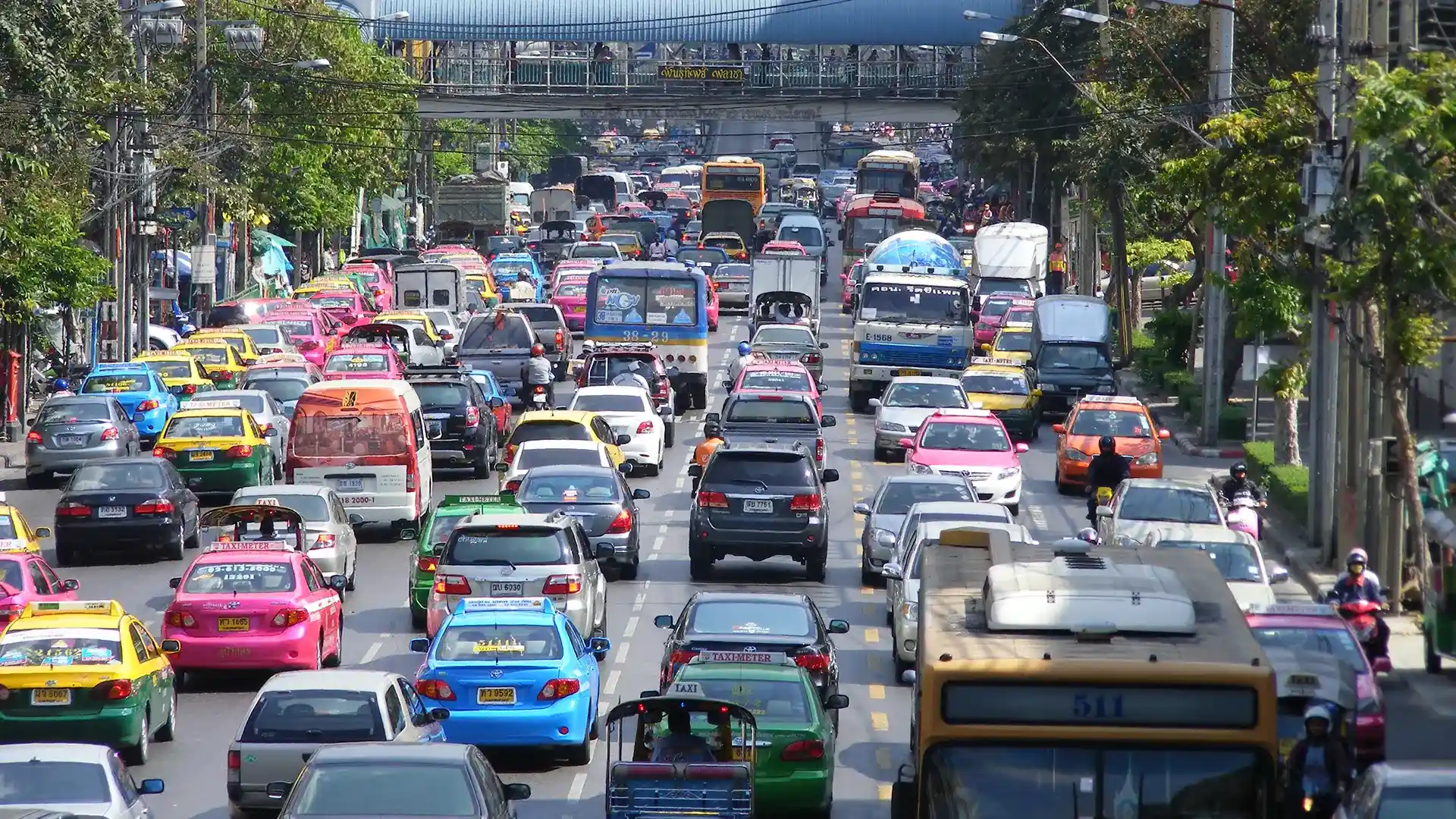 Avenue de Bangkok saturée de taxis multicolores, de bus et d’un tuk-tuk, sous une passerelle piétonne