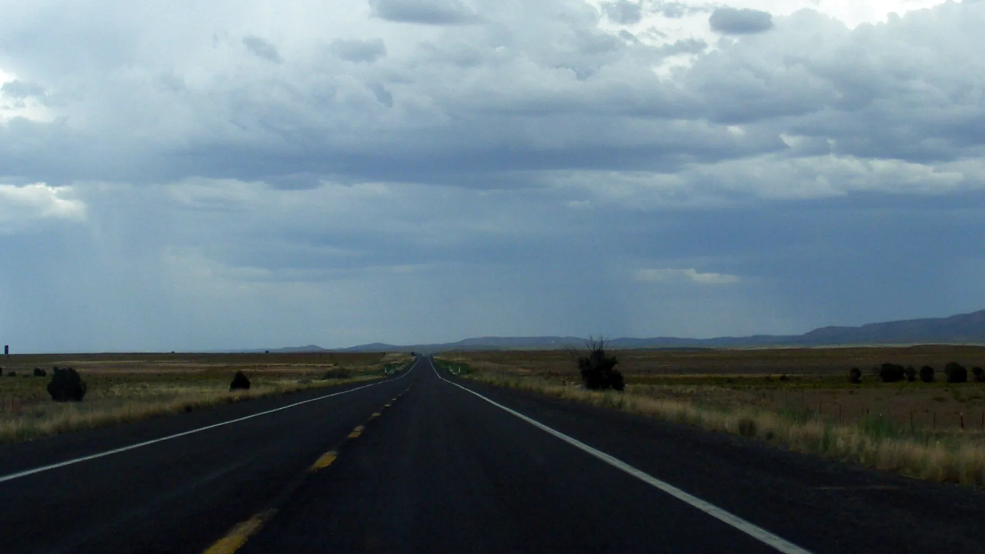 Longue ligne droite d’asphalte filant vers l’horizon sous les nuages d’orage, sur la route du Grand Canyon en Arizona