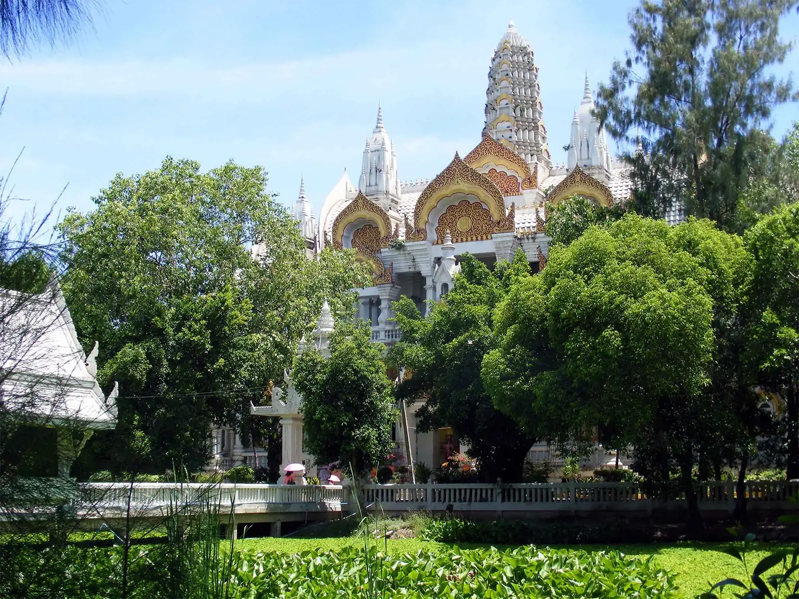 Le Wat Phai Rong Wua à Suphan Buri, ses flèches blanches et dorées émergeant des arbres sous le ciel bleu
